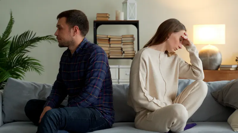 Paar sitzt nachdenklich und voneinander abgewandt auf dem Sofa