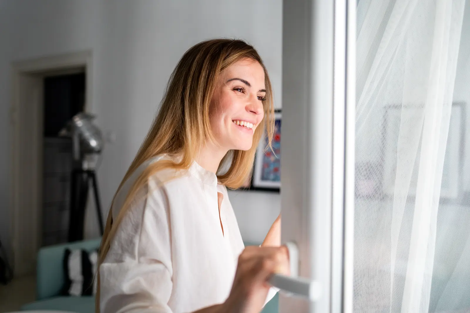 Frau steht lächelnd am offenen Fenster