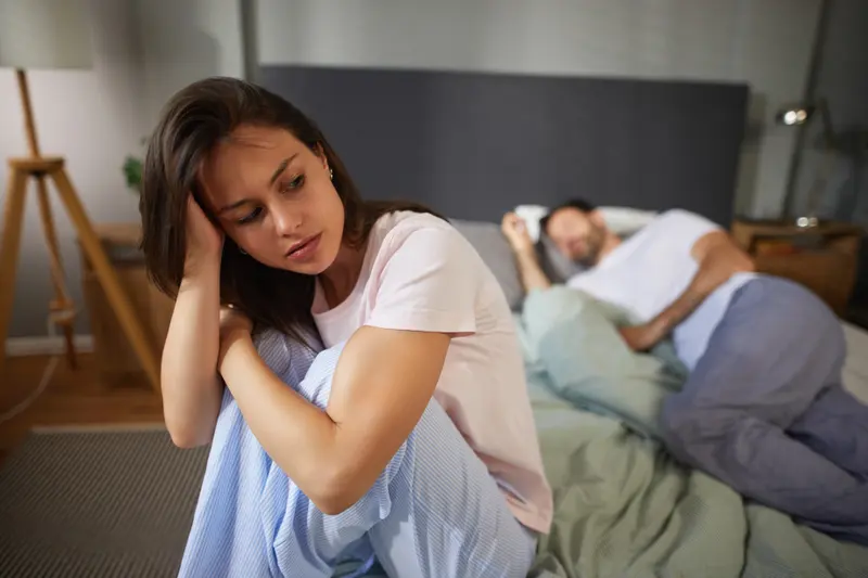 Frau sitzt am Abend wach auf dem Bett, daneben schläft ihr Partner