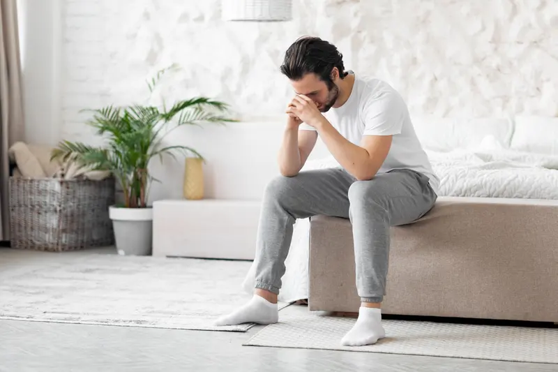 Mann sitzt auf dem Bett und stützt den Kopf in die Hände
